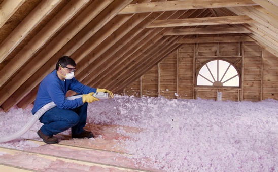 Technician installing pink blown-in insulation in an attic.