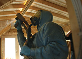 Technician wearing hazmat suit while applying spray foam insulation in a new construction home.