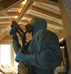 Technician in hazmat suit applying spray foam insulation in an under-construction home.