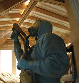 Technician in hazmat suit applying spray foam insulation in a new construction home.
