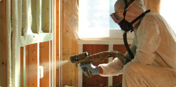 Technician applying spray foam insulation in an unfinished wall while wearing a hazmat suit.