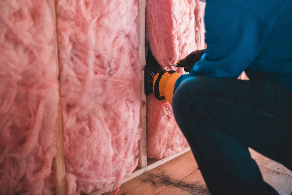 Technician installing pink fiberglass insulation in a wall.