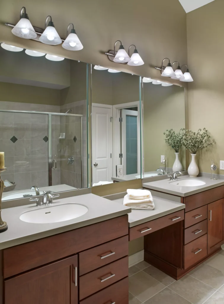Custom set of three large mirrors installed in a home's bathroom with dual vanity, light gray countertop, and woodgrain cabinets and drawers. Pale beige wall.