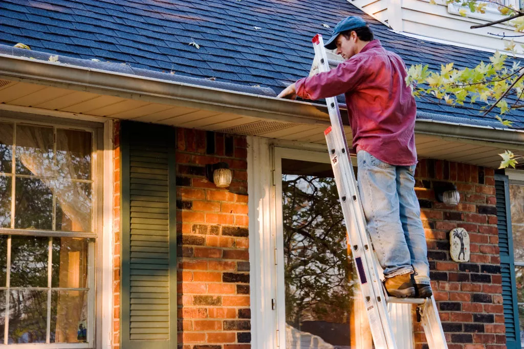 Technician on ladder installing gutters on a brick home.